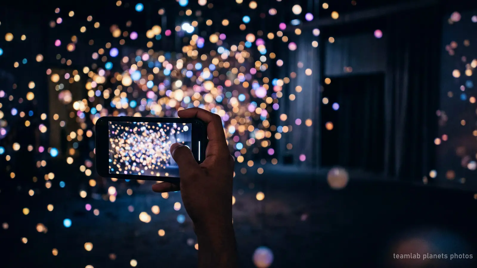 Illustration : un téléphone photographiant une salle sombre de lumière colorée, le genre de photo que prennent les visiteurs de teamLab Planets
